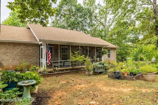 back of house featuring a sunroom, a shingled roof, a garden, and brick siding