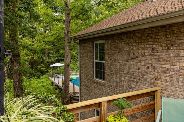 exterior space with brick siding, roof with shingles, and an outdoor pool