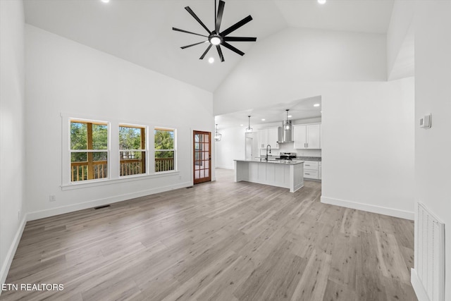 unfurnished living room featuring high vaulted ceiling, light wood-style flooring, a sink, a ceiling fan, and baseboards