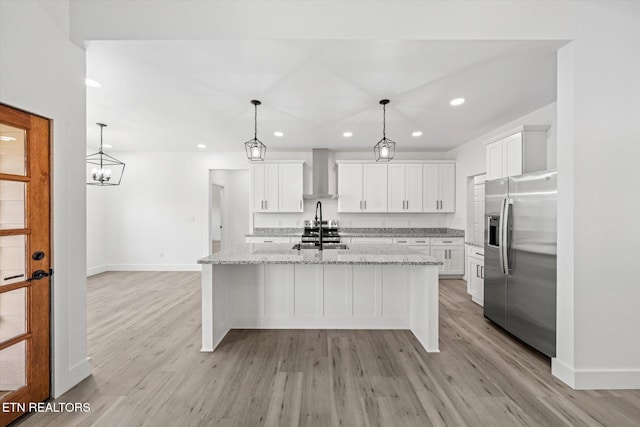 kitchen with wall chimney exhaust hood, stainless steel fridge, light wood-style flooring, and white cabinetry