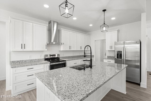 kitchen featuring a center island with sink, white cabinets, appliances with stainless steel finishes, wall chimney range hood, and a sink