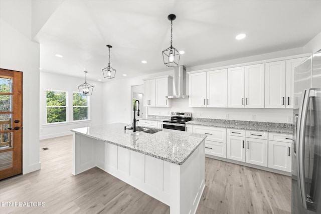 kitchen featuring light wood-style flooring, stainless steel appliances, a sink, white cabinets, and wall chimney range hood