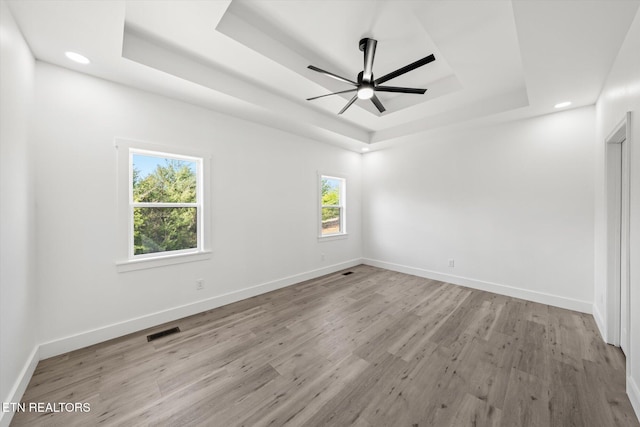 empty room featuring plenty of natural light, a raised ceiling, visible vents, and baseboards