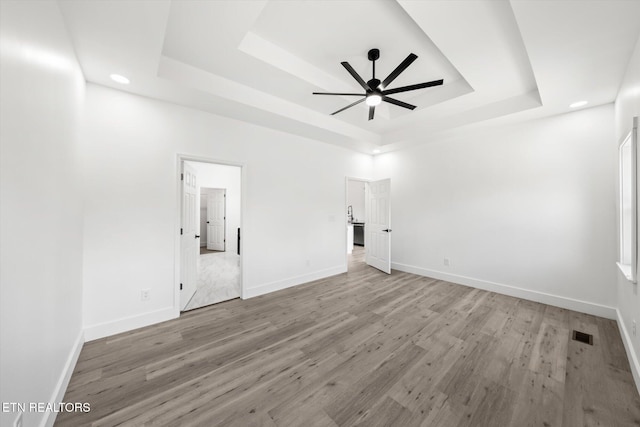 unfurnished bedroom with wood finished floors, a raised ceiling, visible vents, and baseboards