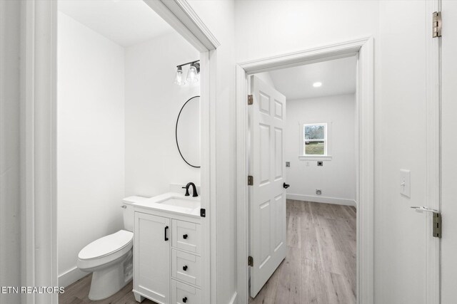 half bath with toilet, baseboards, wood finished floors, and vanity