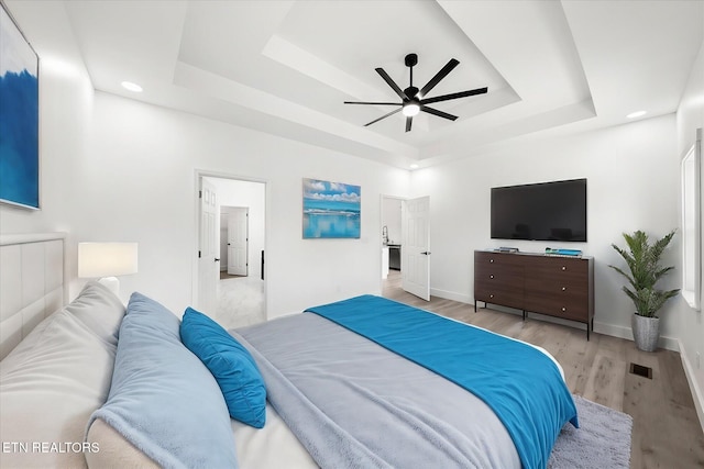 bedroom with visible vents, baseboards, a raised ceiling, a ceiling fan, and light wood-style floors