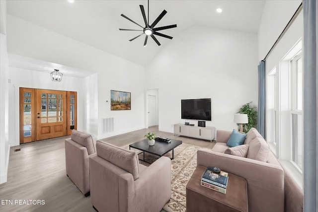 living room featuring high vaulted ceiling, light wood finished floors, visible vents, and baseboards