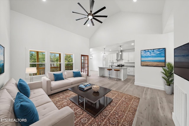 living area with recessed lighting, light wood-style floors, a ceiling fan, high vaulted ceiling, and baseboards