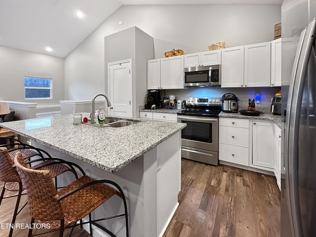 kitchen featuring white cabinets, dark wood finished floors, a breakfast bar, stainless steel appliances, and a sink