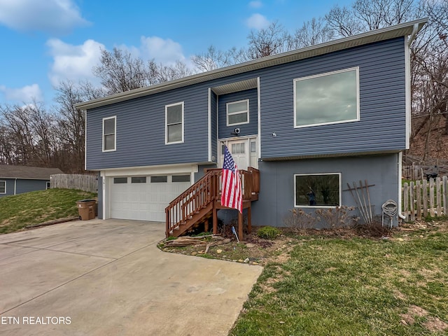 bi-level home with a front yard, concrete driveway, fence, and an attached garage