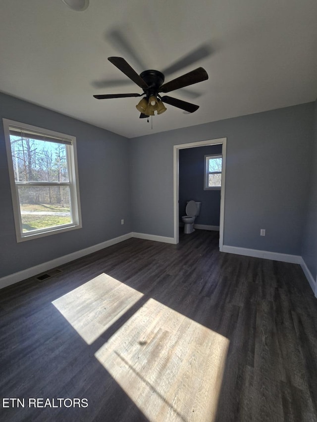 unfurnished bedroom with dark wood-style floors, multiple windows, and baseboards