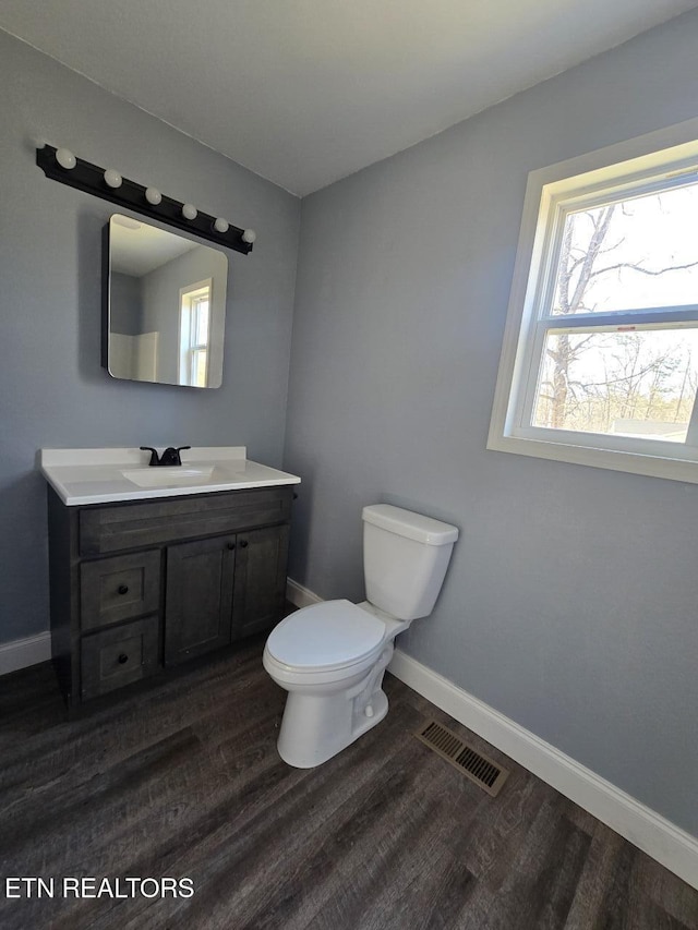 half bath featuring visible vents, toilet, vanity, wood finished floors, and baseboards