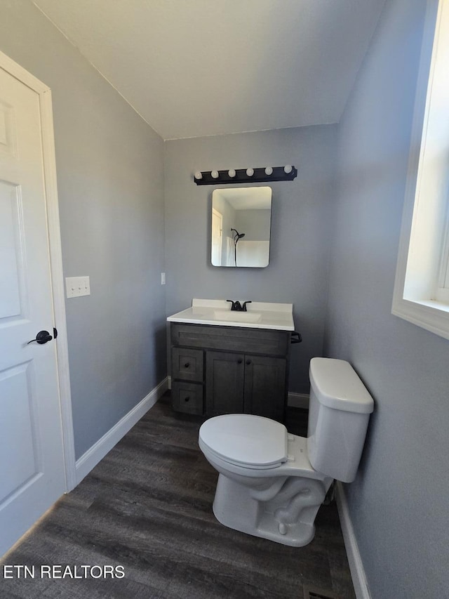 bathroom with baseboards, toilet, wood finished floors, vaulted ceiling, and vanity