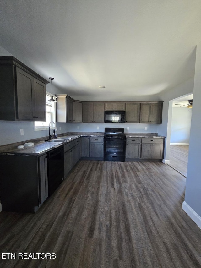 kitchen with hanging light fixtures, dark wood-type flooring, a sink, black appliances, and baseboards