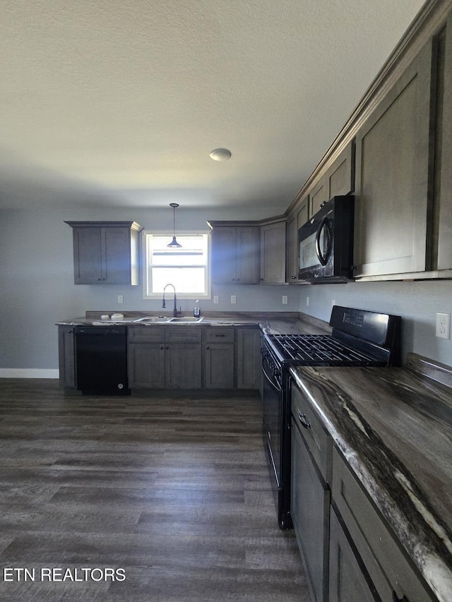 kitchen featuring a textured ceiling, a sink, dark wood-style floors, black appliances, and pendant lighting