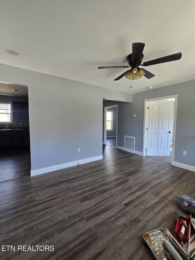 unfurnished living room featuring a ceiling fan, dark wood-style flooring, visible vents, and baseboards