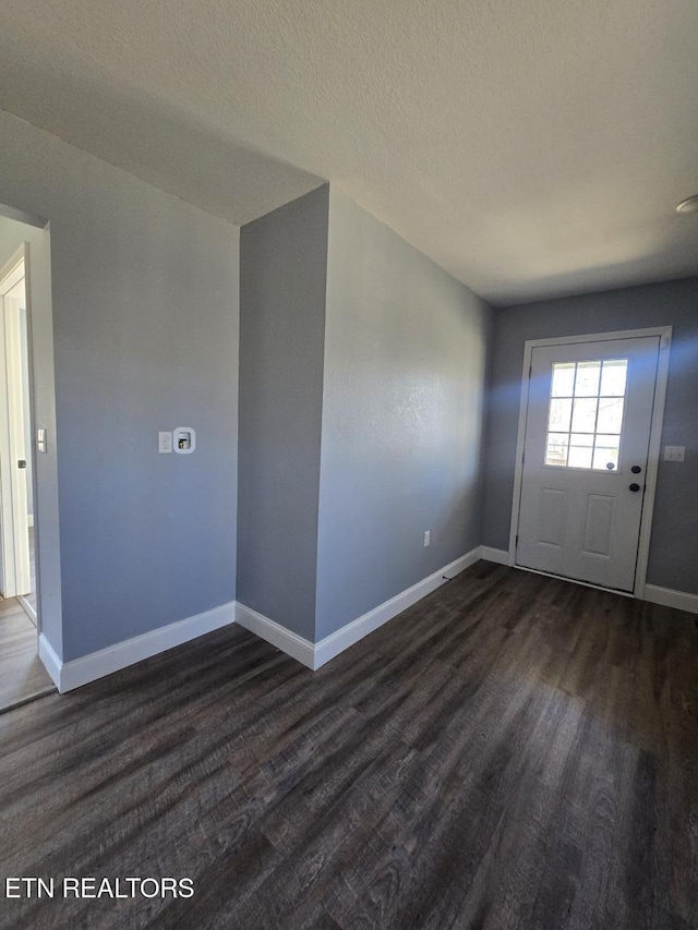 foyer entrance featuring dark wood finished floors, a textured ceiling, and baseboards