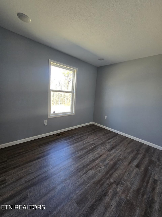 spare room with dark wood-style floors, baseboards, visible vents, and a textured ceiling