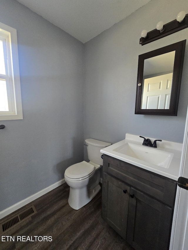 half bathroom featuring visible vents, toilet, vanity, wood finished floors, and baseboards