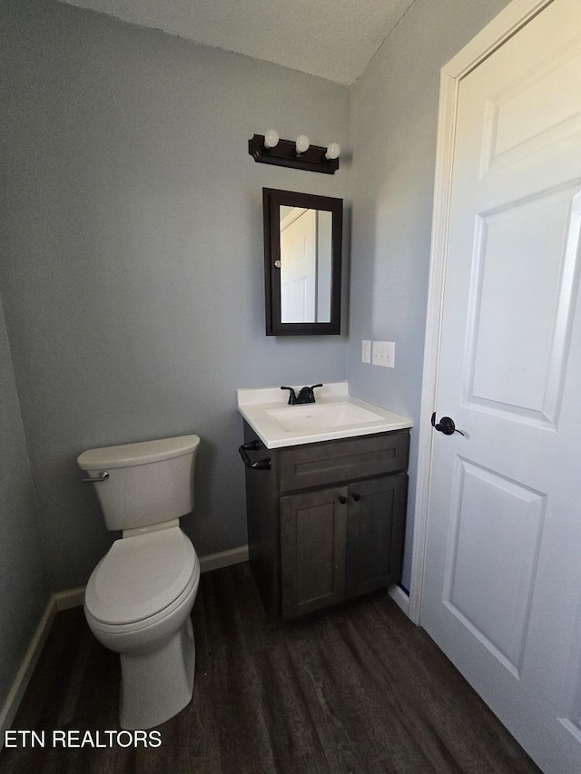 half bathroom featuring toilet, vanity, baseboards, and wood finished floors