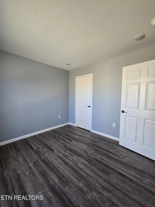 unfurnished bedroom with a textured ceiling, baseboards, and dark wood-type flooring