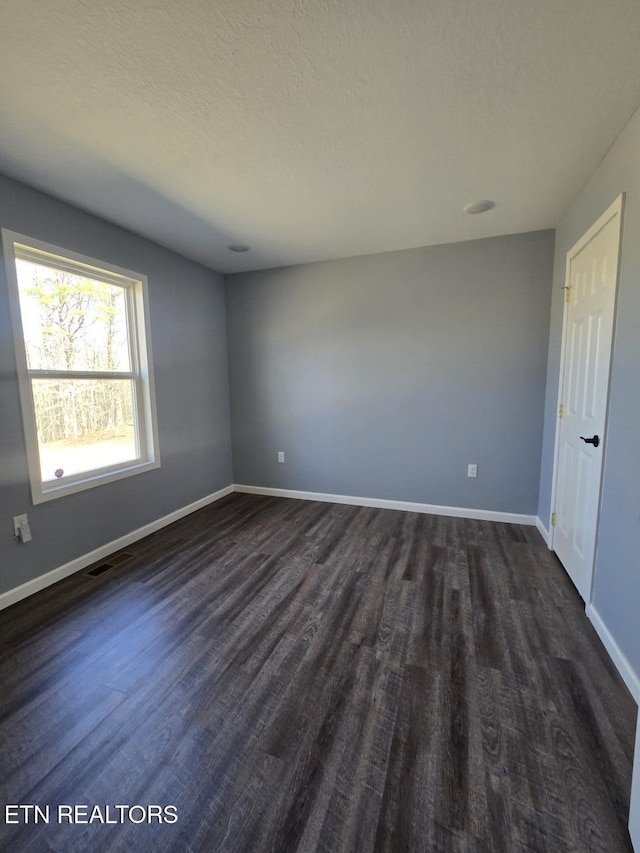 empty room with dark wood-style floors, visible vents, a textured ceiling, and baseboards