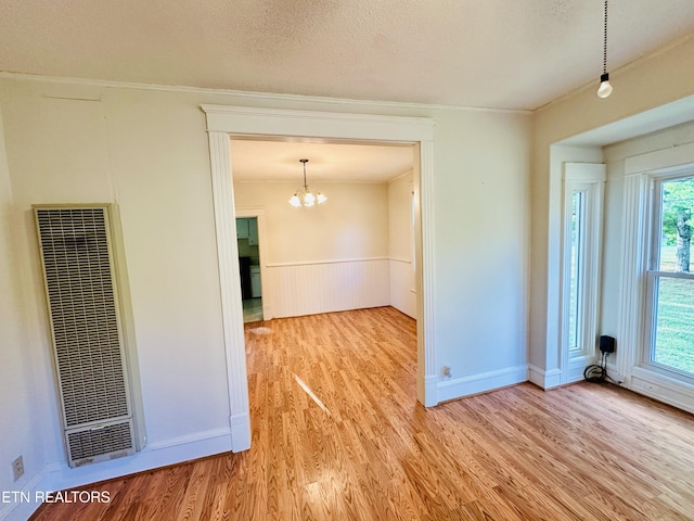 empty room with a chandelier, light wood finished floors, a heating unit, and crown molding