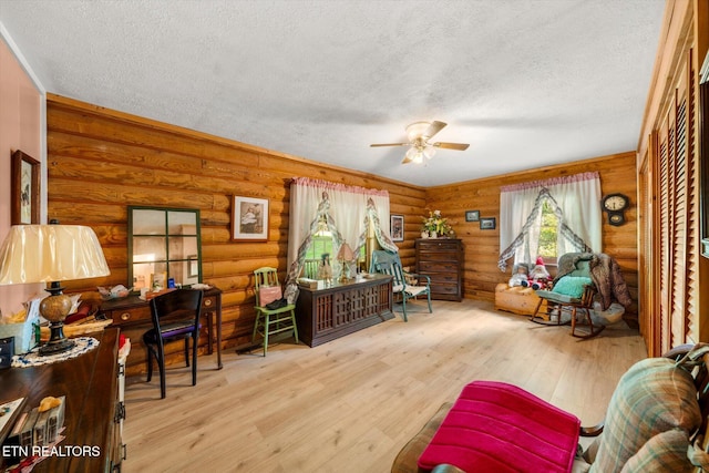 interior space with a textured ceiling, ceiling fan, wood finished floors, and log walls