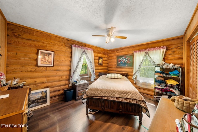 bedroom with a textured ceiling, log walls, wood finished floors, and a ceiling fan