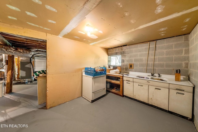 kitchen with concrete flooring, light countertops, a sink, and concrete block wall