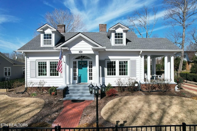 cape cod-style house featuring roof with shingles, a chimney, and fence