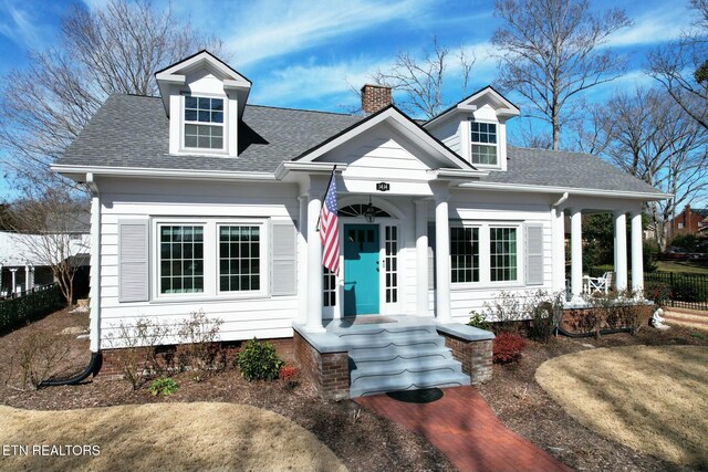 cape cod house with a shingled roof, a chimney, and fence