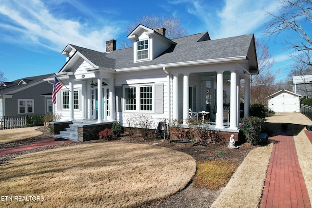 view of front of home featuring an outbuilding, a porch, roof with shingles, a front lawn, and a chimney