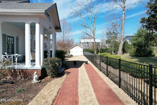 exterior space with a shingled roof, covered porch, fence, and an outdoor structure