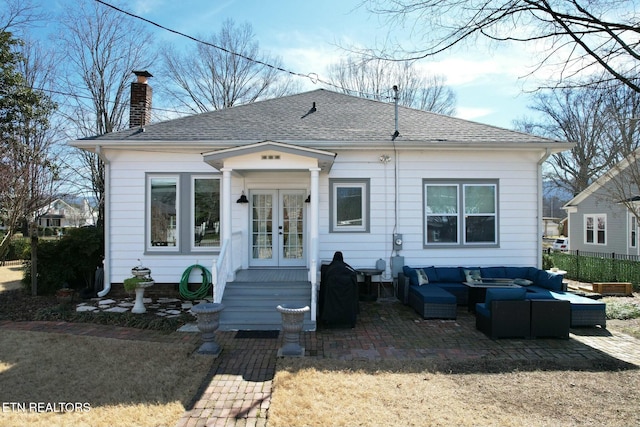 bungalow-style home with a patio, an outdoor living space, french doors, roof with shingles, and a chimney