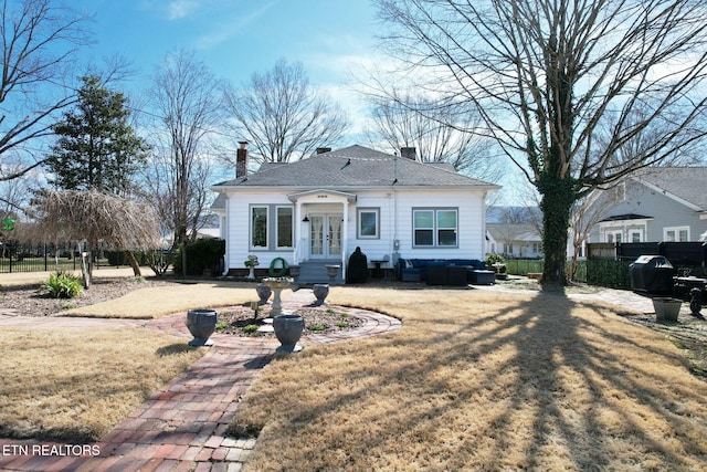 bungalow-style home with a shingled roof, fence, french doors, a chimney, and a front yard