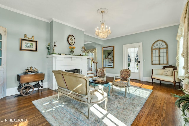 living area with a fireplace, wood finished floors, baseboards, an inviting chandelier, and crown molding