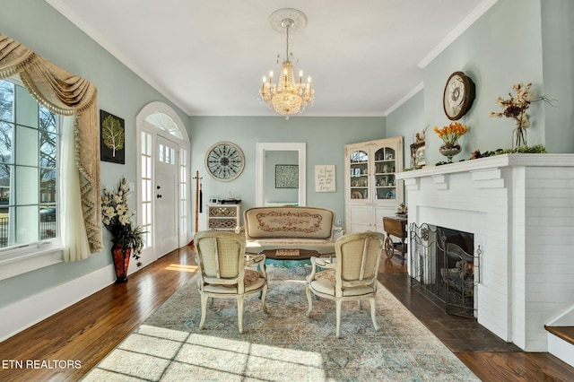 living area featuring dark wood-style floors, ornamental molding, a brick fireplace, and an inviting chandelier