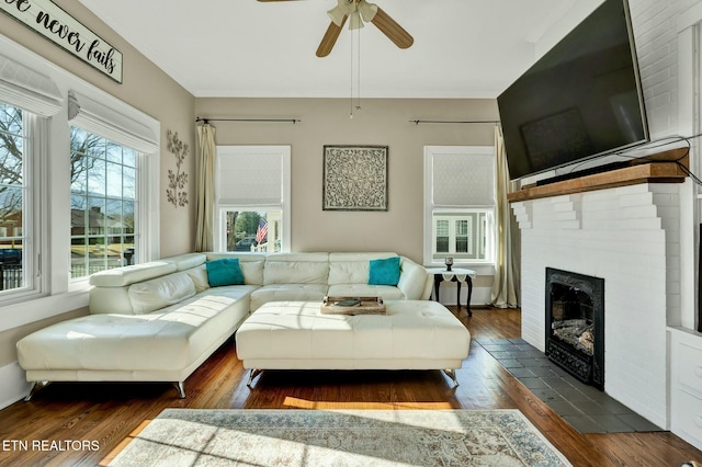 living area featuring wood-type flooring, a fireplace, a ceiling fan, and crown molding