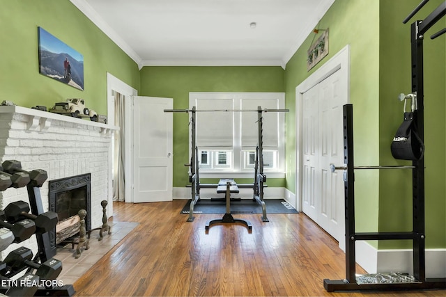 workout room featuring crown molding, a fireplace, baseboards, and wood finished floors