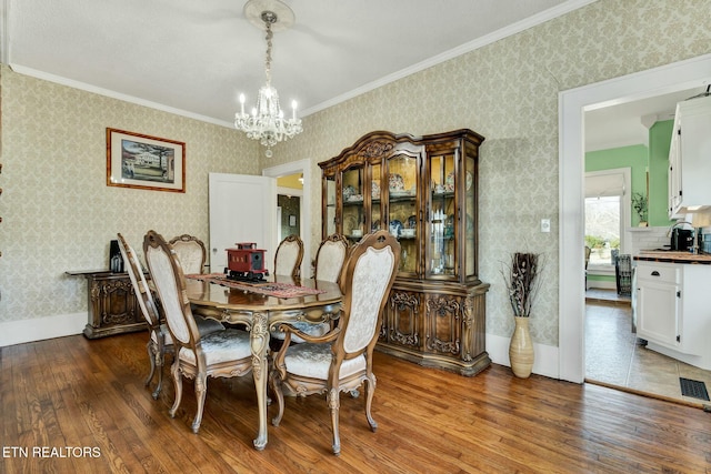 dining space featuring wallpapered walls, baseboards, hardwood / wood-style floors, crown molding, and a notable chandelier