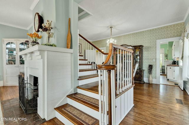 stairs with wallpapered walls, baseboards, hardwood / wood-style flooring, crown molding, and a chandelier