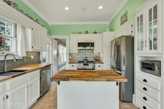 kitchen with appliances with stainless steel finishes, white cabinetry, wooden counters, and crown molding