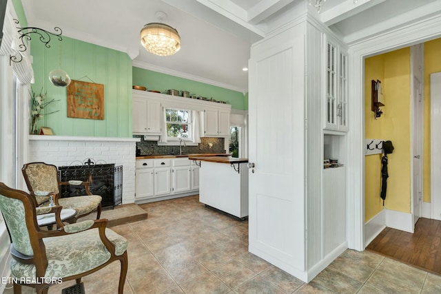 kitchen with butcher block counters, a sink, white cabinetry, ornamental molding, and tasteful backsplash