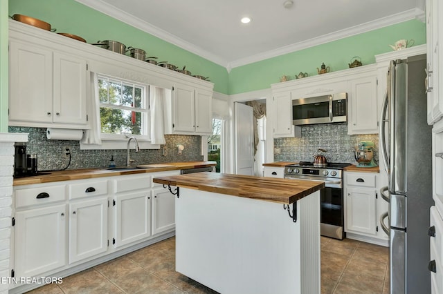 kitchen with a center island, crown molding, stainless steel appliances, butcher block counters, and white cabinetry