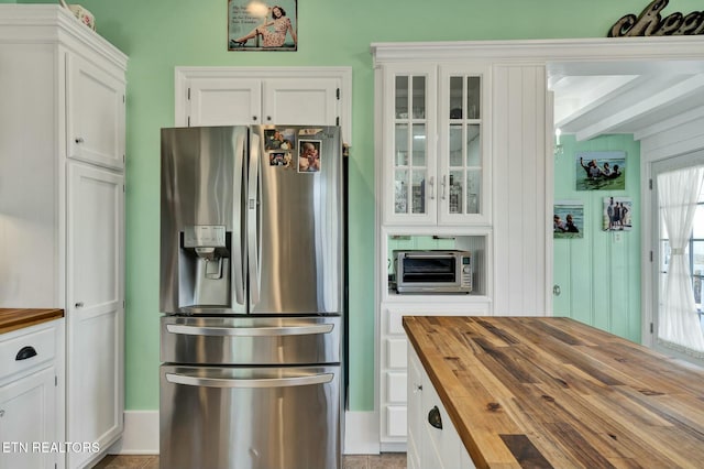 kitchen with glass insert cabinets, stainless steel fridge, wooden counters, and white cabinetry