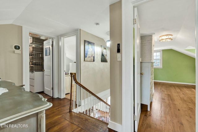 hallway with baseboards, vaulted ceiling, dark wood-type flooring, and an upstairs landing