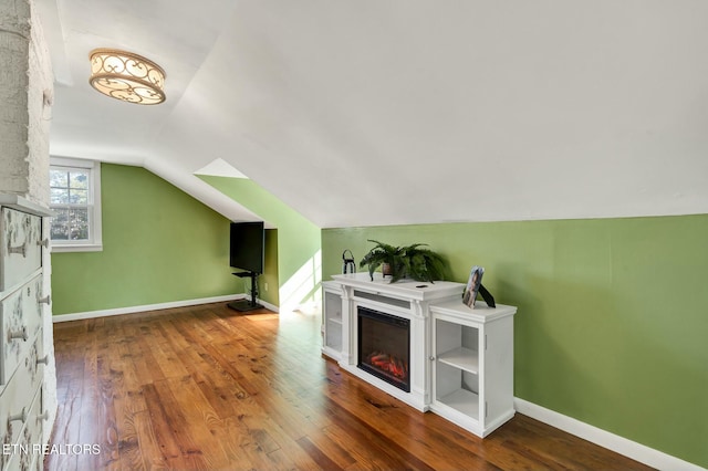 bonus room with baseboards, vaulted ceiling, hardwood / wood-style floors, and a glass covered fireplace