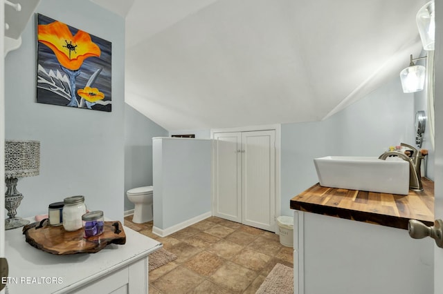 bathroom with toilet, baseboards, a sink, and lofted ceiling