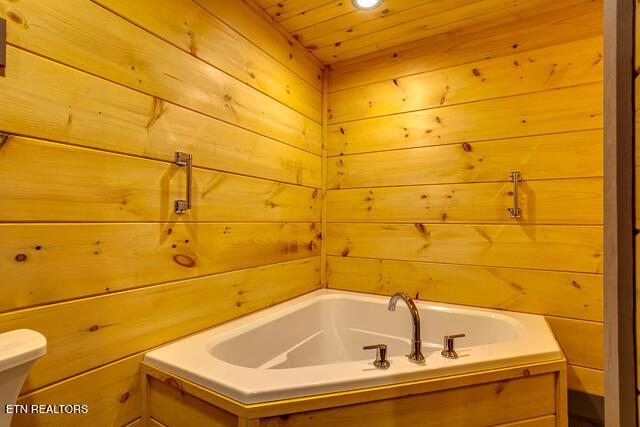 bathroom featuring toilet, wood walls, wood ceiling, and a bath